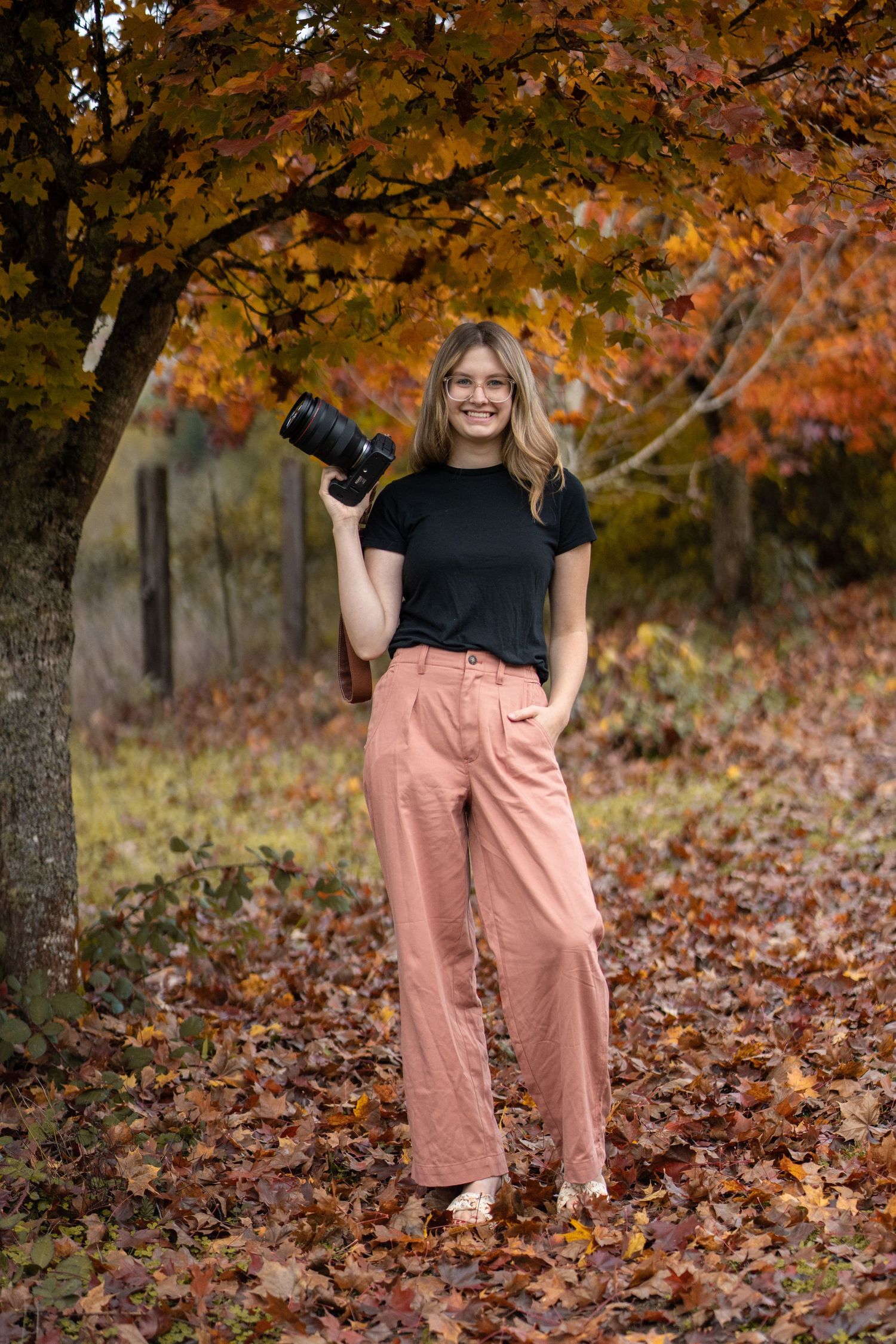 Professional photographer in autumn setting holding camera against colorful fall foliage.