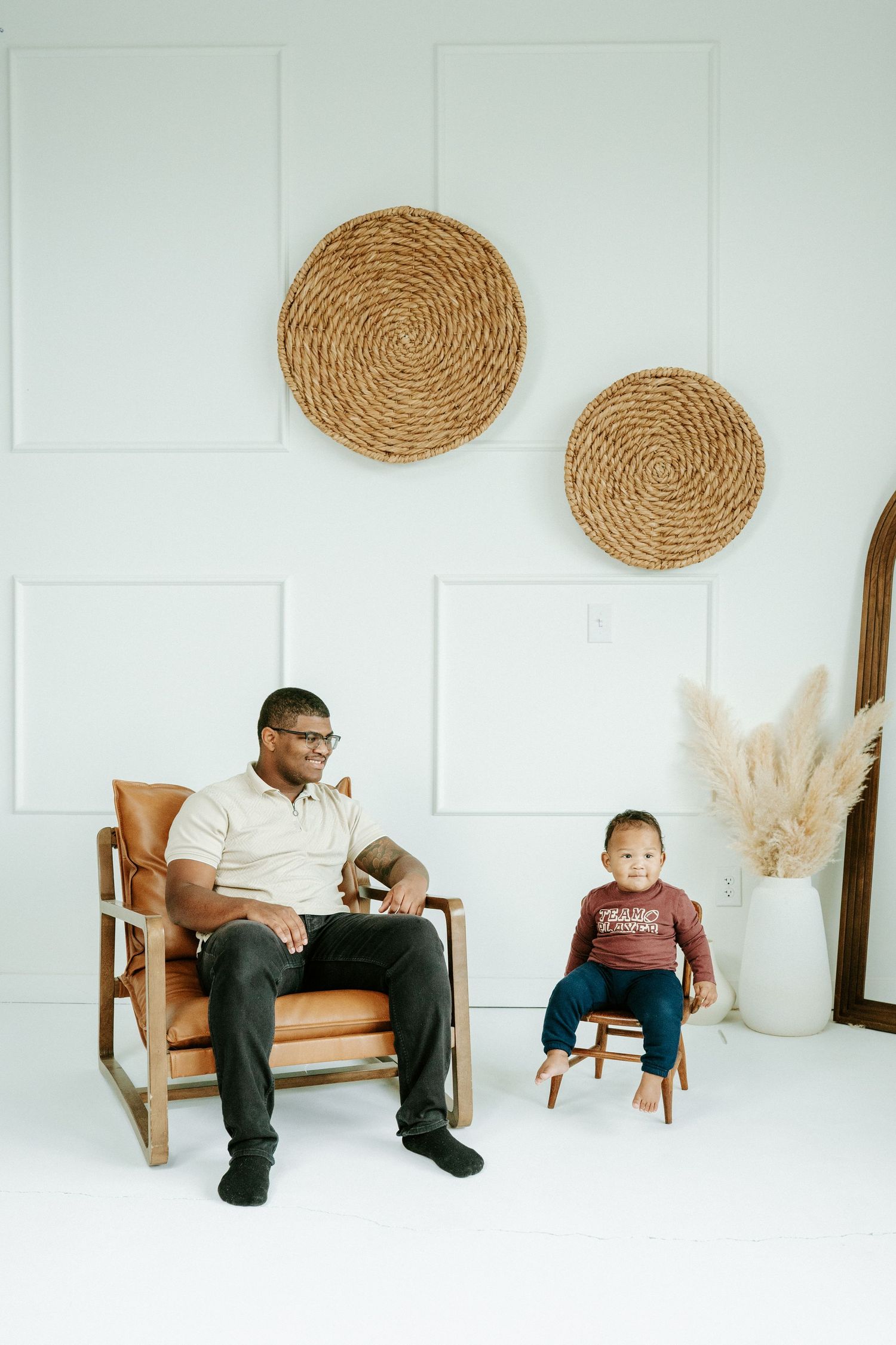 Minimalist white studio photo sequence showing a wooden chair and woven wall decor with pampas grass arrangement.
