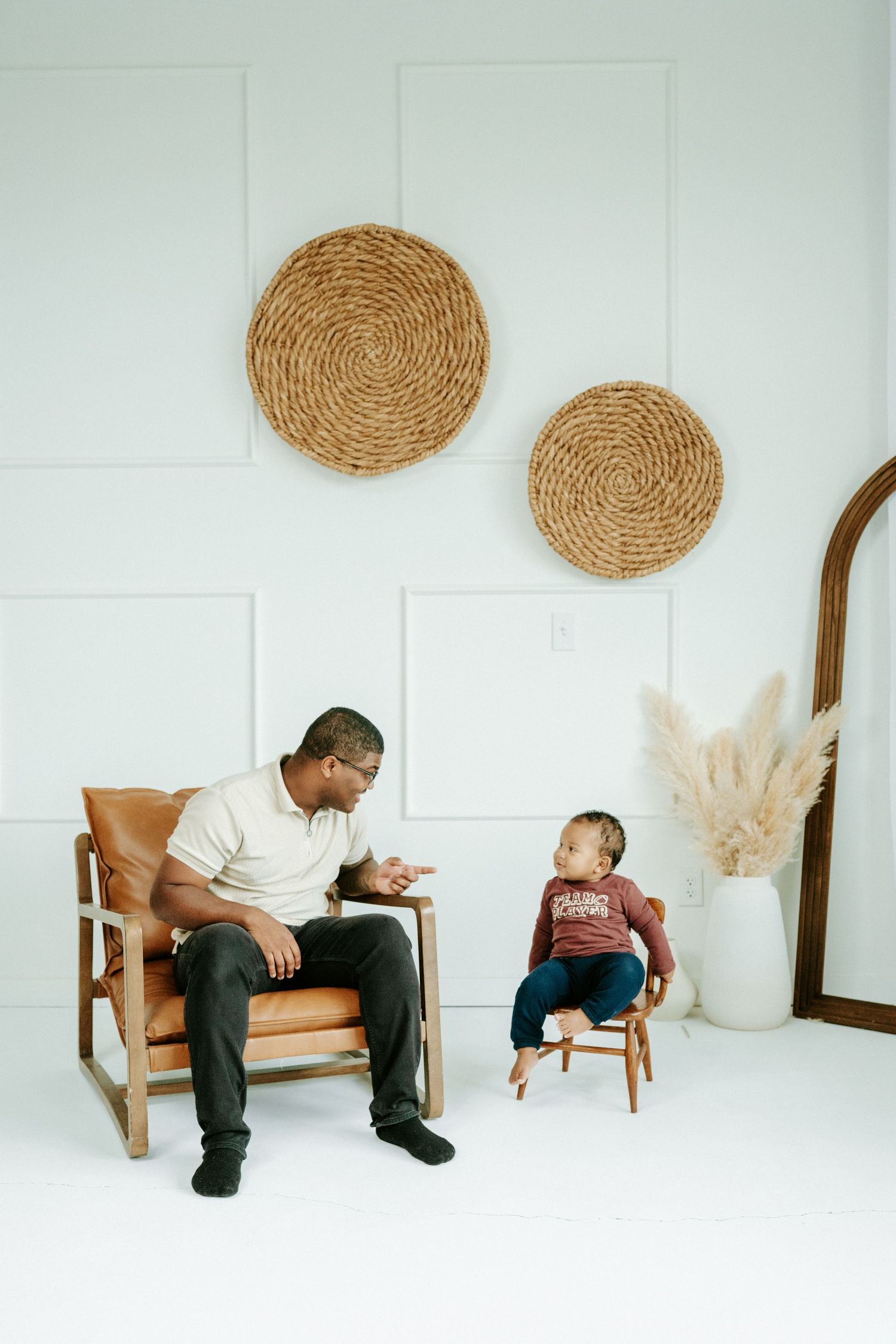 A progressive series of photos showing two people sitting on a chair against a white wall with woven circle decor.