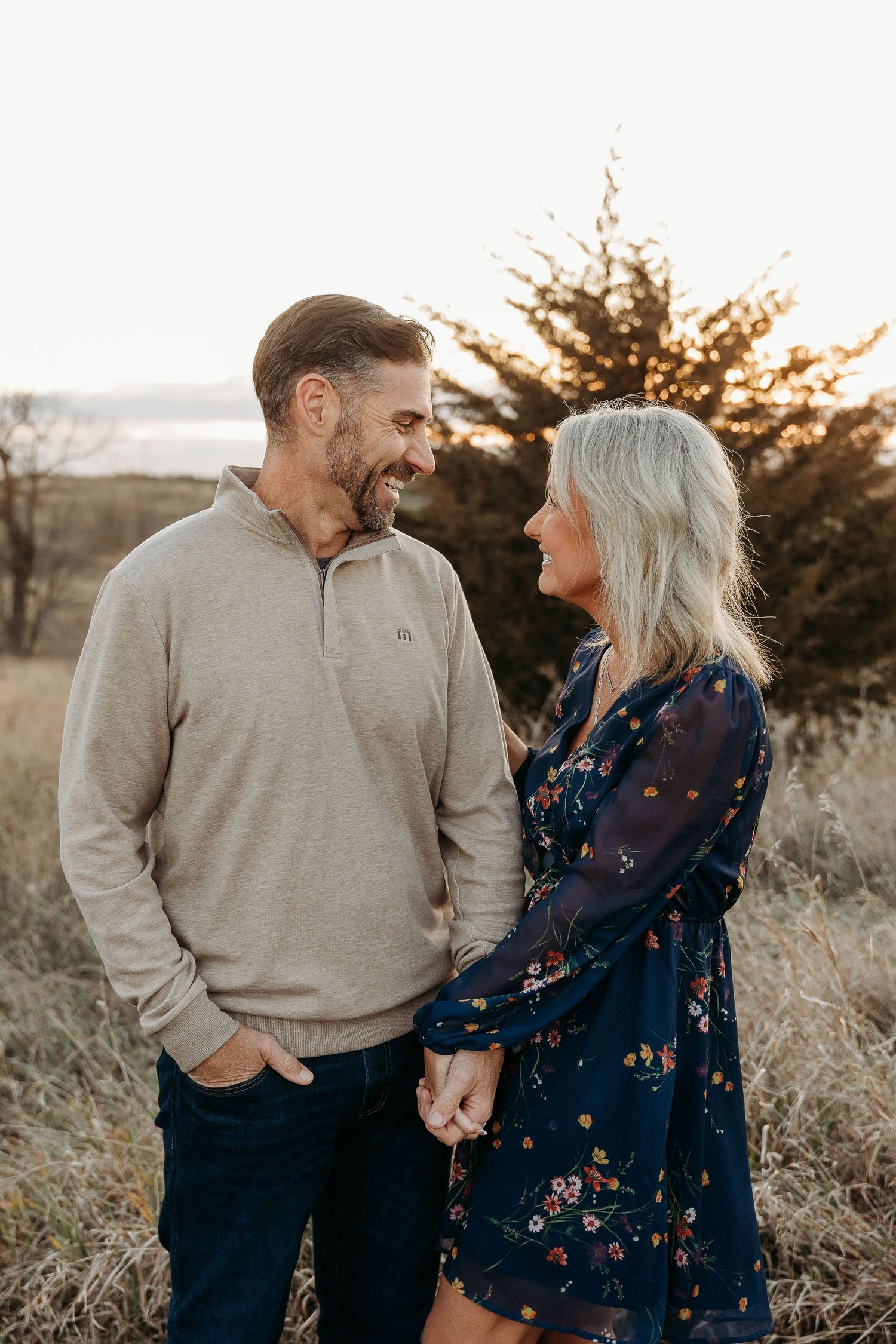 A couple shares tender moments in a field at sunset wearing casual attire and embracing each other warmly.