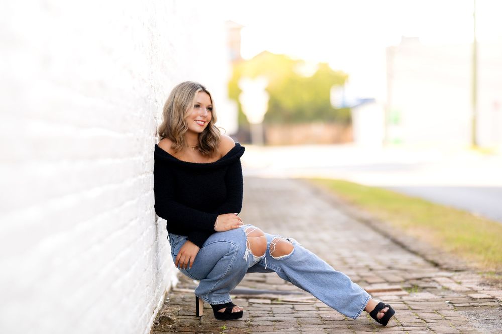 Person in black sweater and blue jeans posing casually on stone steps in outdoor setting.