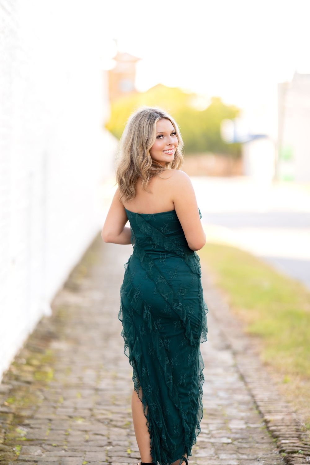 Woman in elegant teal ruffled dress poses on cobblestone path during golden hour photoshoot.