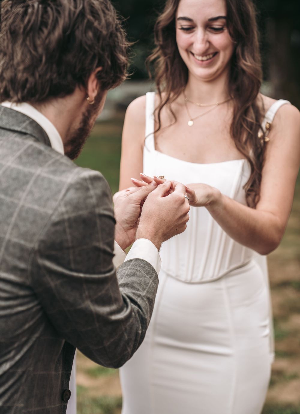 Groom placing wedding ring on bride's finger during ceremony, bride smiling in white dress.