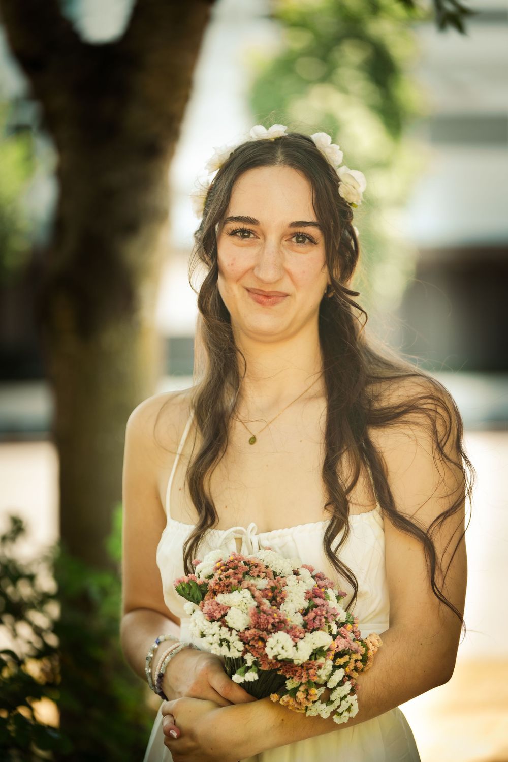 Smiling bride in white dress holding pink and white flower bouquet with floral crown in her hair.