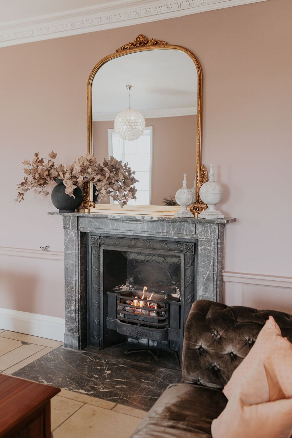 Pink living room with marble fireplace, gold mirror, and velvet sofa.