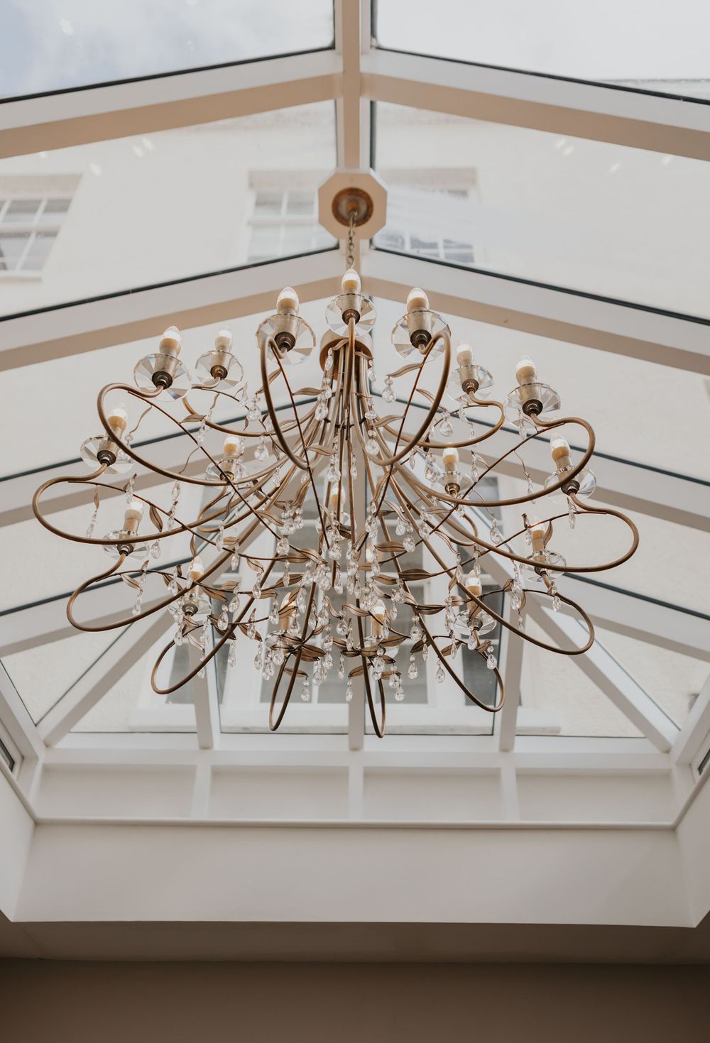 Ornate gold and crystal chandelier hanging beneath glass atrium ceiling.
