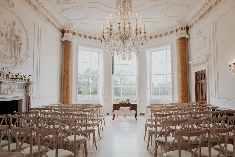 Grand oval wedding ceremony room with crystal chandelier and crossback chairs.