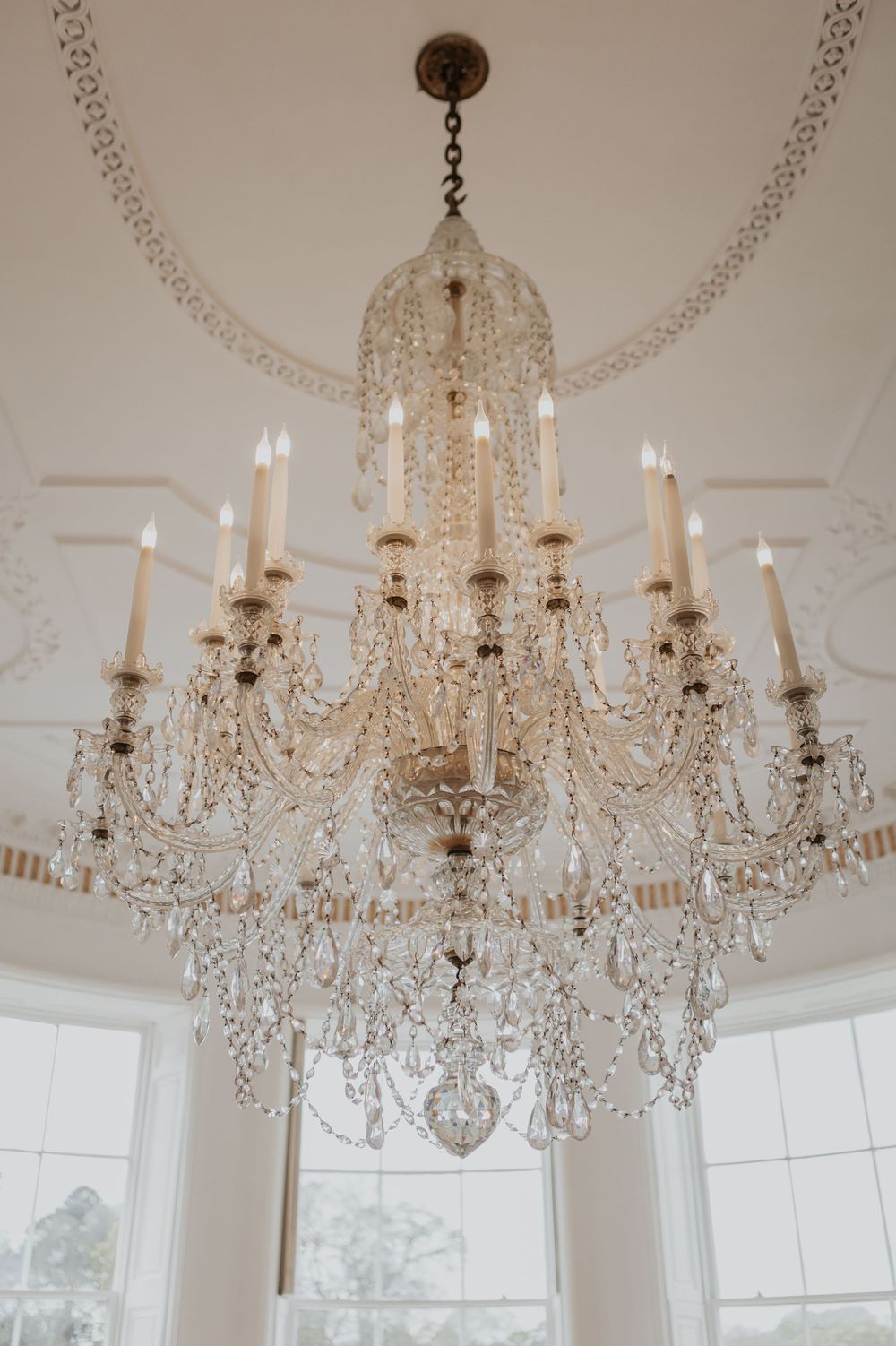 Large crystal chandelier with candle lights in ornate white plasterwork ceiling.
