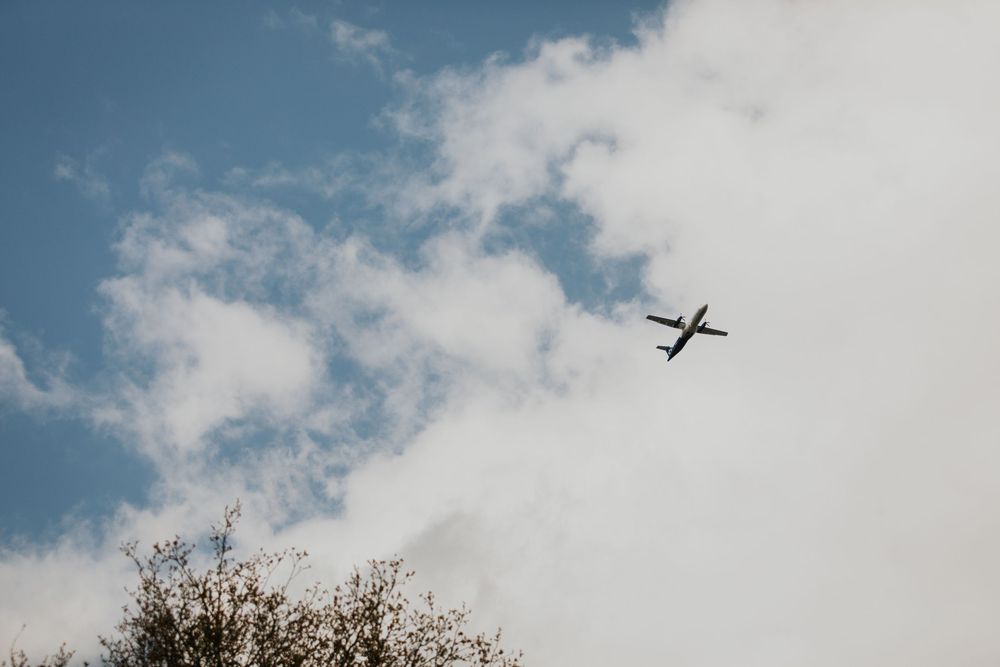 Commercial airplane flying through blue sky with white clouds above treetops.