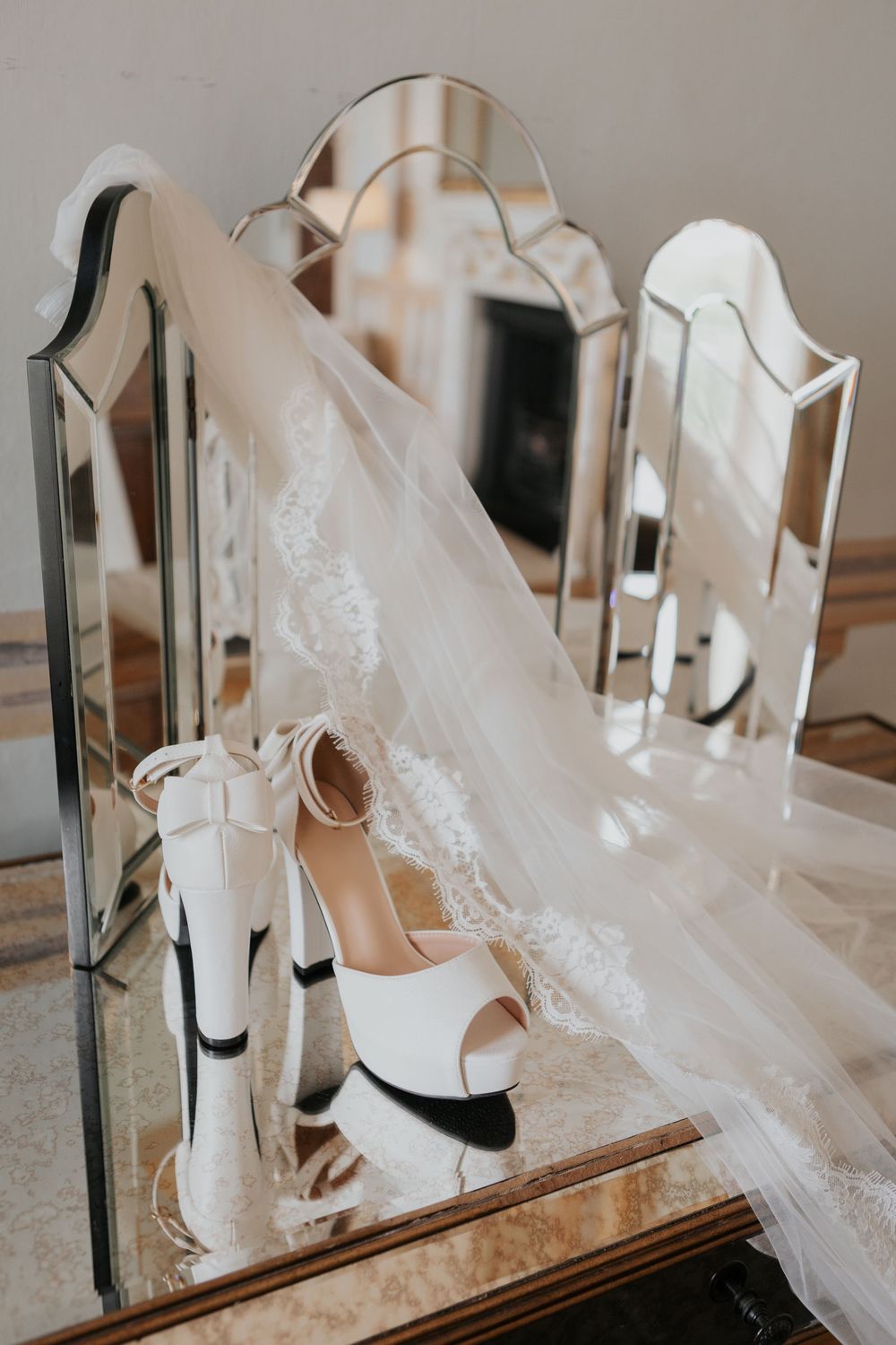 White bridal heels and lace veil reflected in vintage trifold vanity mirror.