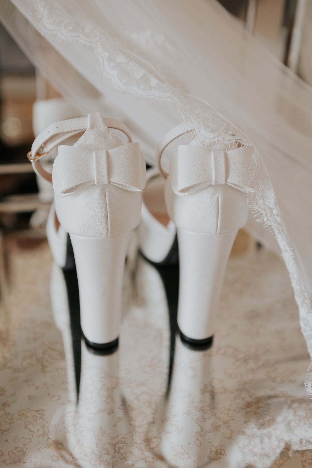 White bridal heels with bow detail photographed from behind beneath a lace wedding veil.