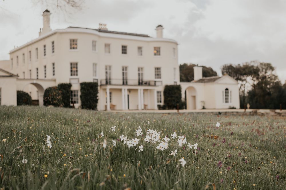 White Georgian manor house with spring daffodils blooming in foreground meadow.