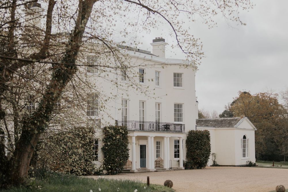Elegant white Georgian country house surrounded by mature trees and gravel driveway.