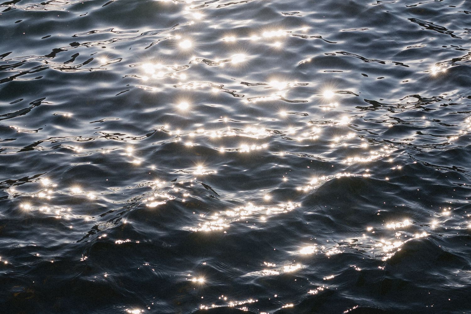 Sunlight sparkles across dark rippling ocean waves creating a mesmerizing pattern of reflections on the water's surface.