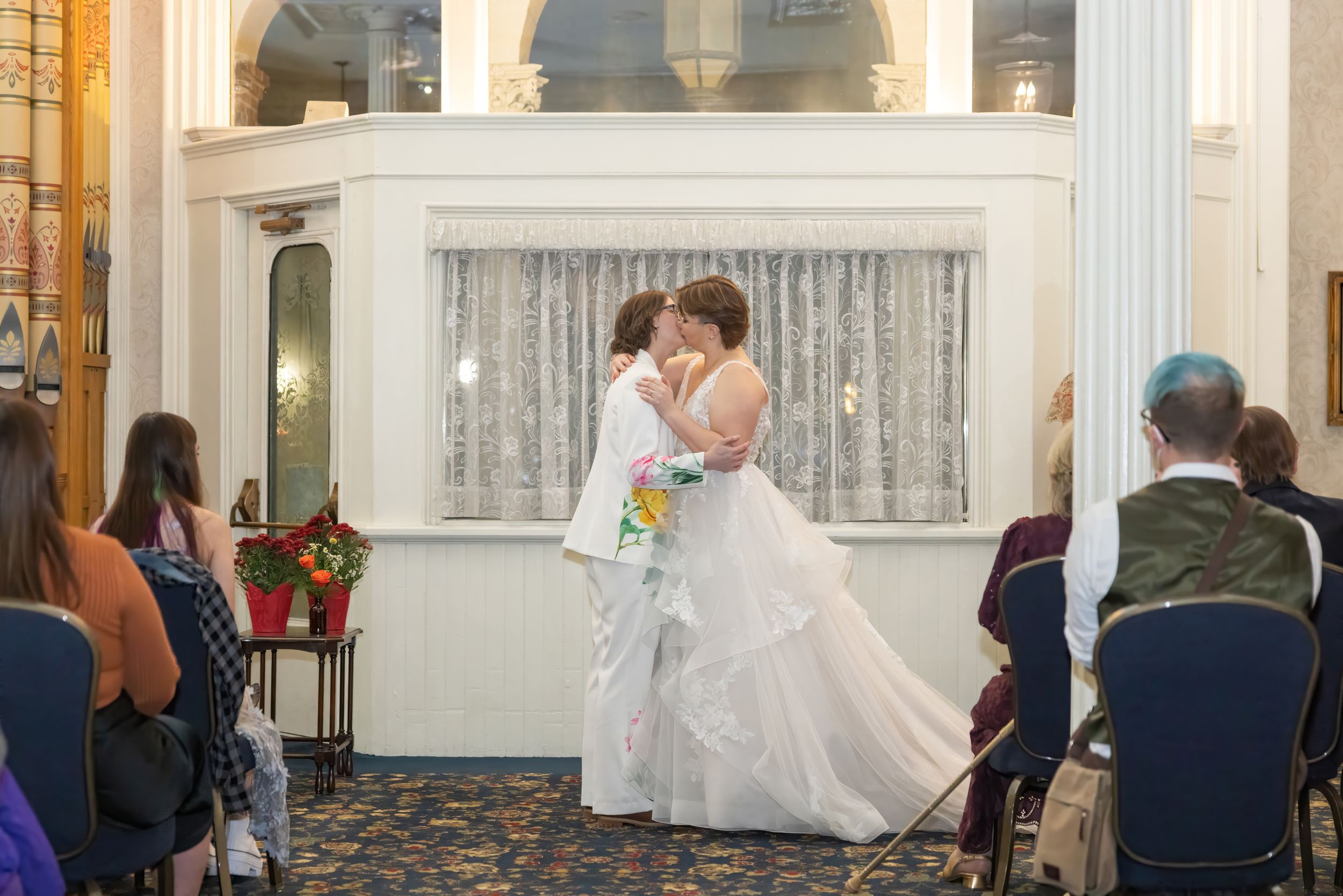 A wedding reception venue shows multiple guests seated at tables while a couple dances in an elegant white room.