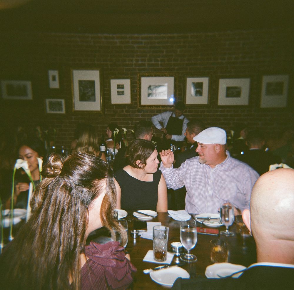 Vintage-style film photos showing people gathered at tables in a dimly lit room during a social event.
