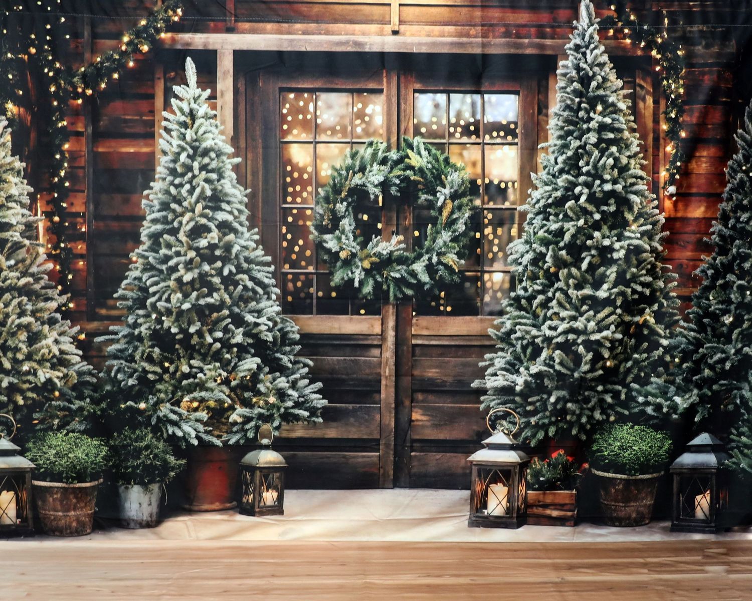 Snow-covered Christmas trees flanking wooden door with wreath and lantern decorations.