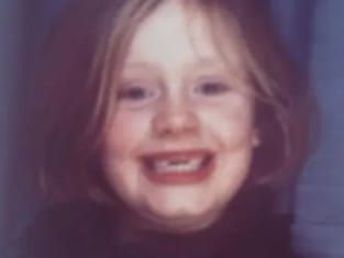 A blurry vintage photograph shows a smiling child with light hair against a dark background.