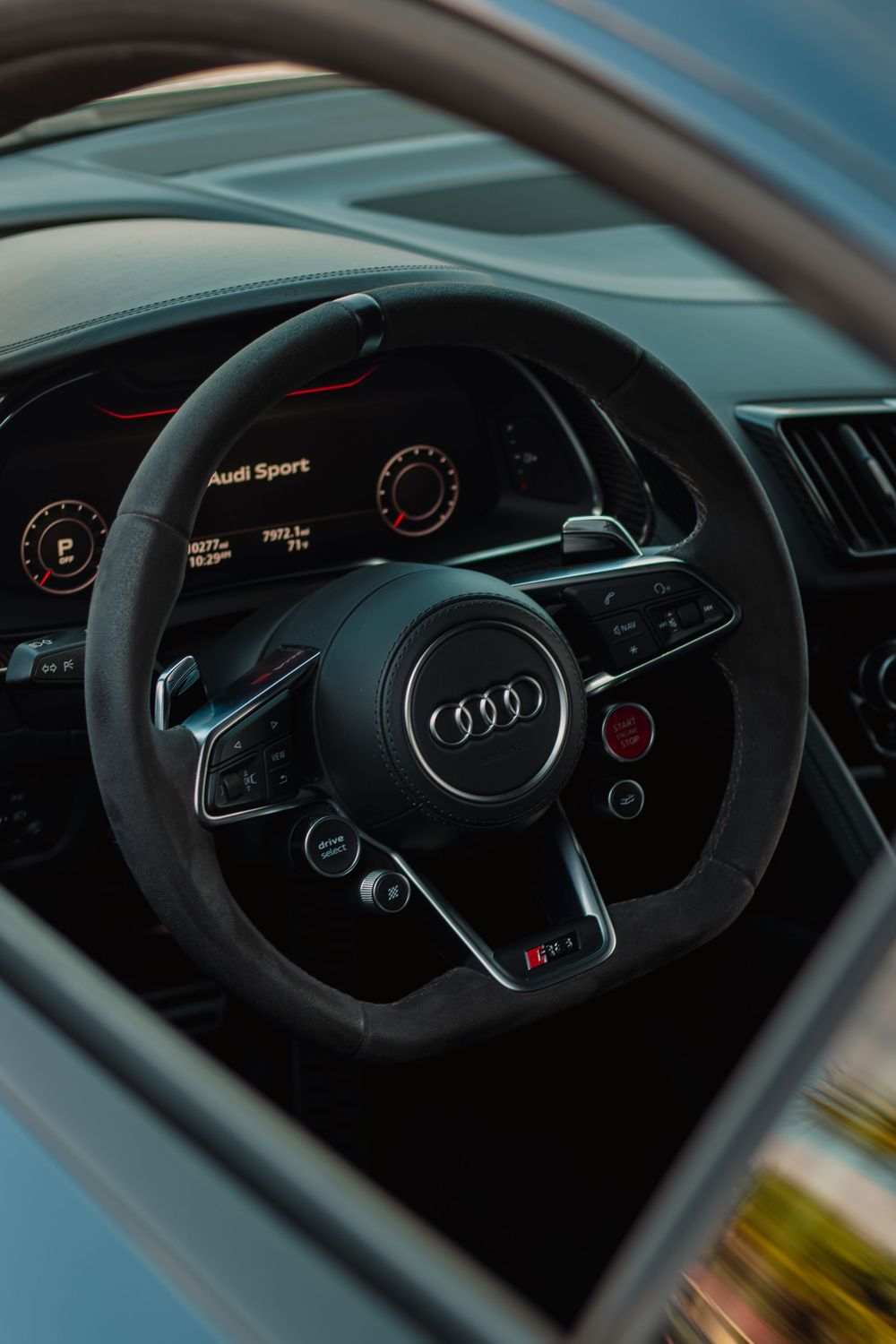 Interior dashboard view of an Audi vehicle showing the steering wheel and digital instrument cluster with sport branding.
