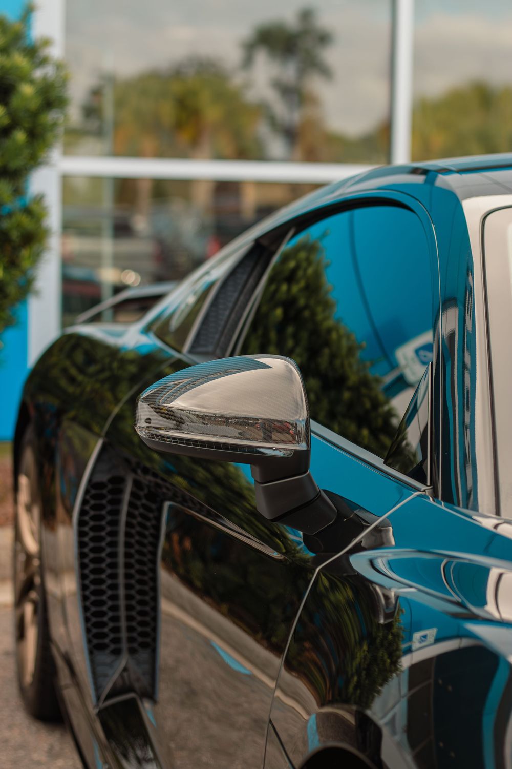 Close-up view of black side mirror details on a blue car exterior showing reflective surfaces and modern design elements.