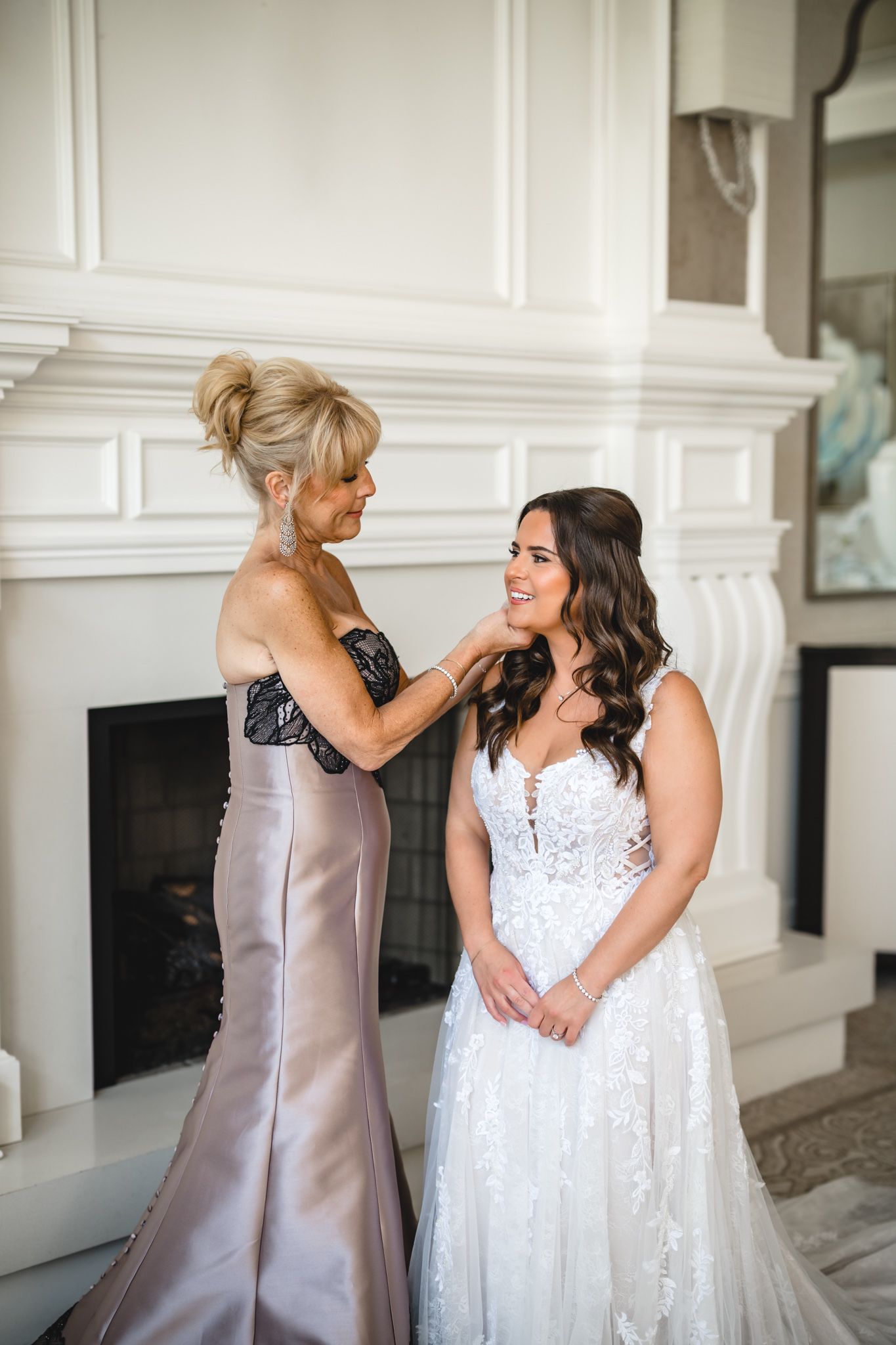 A touching pre-wedding moment between two women in elegant dresses by a fireplace.