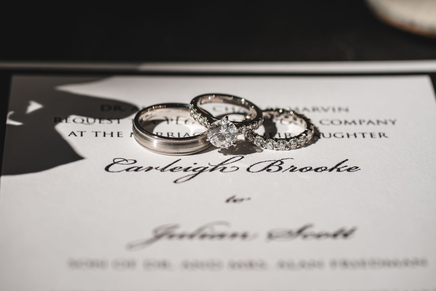 Wedding rings photographed on top of elegant wedding invitation in black and white.