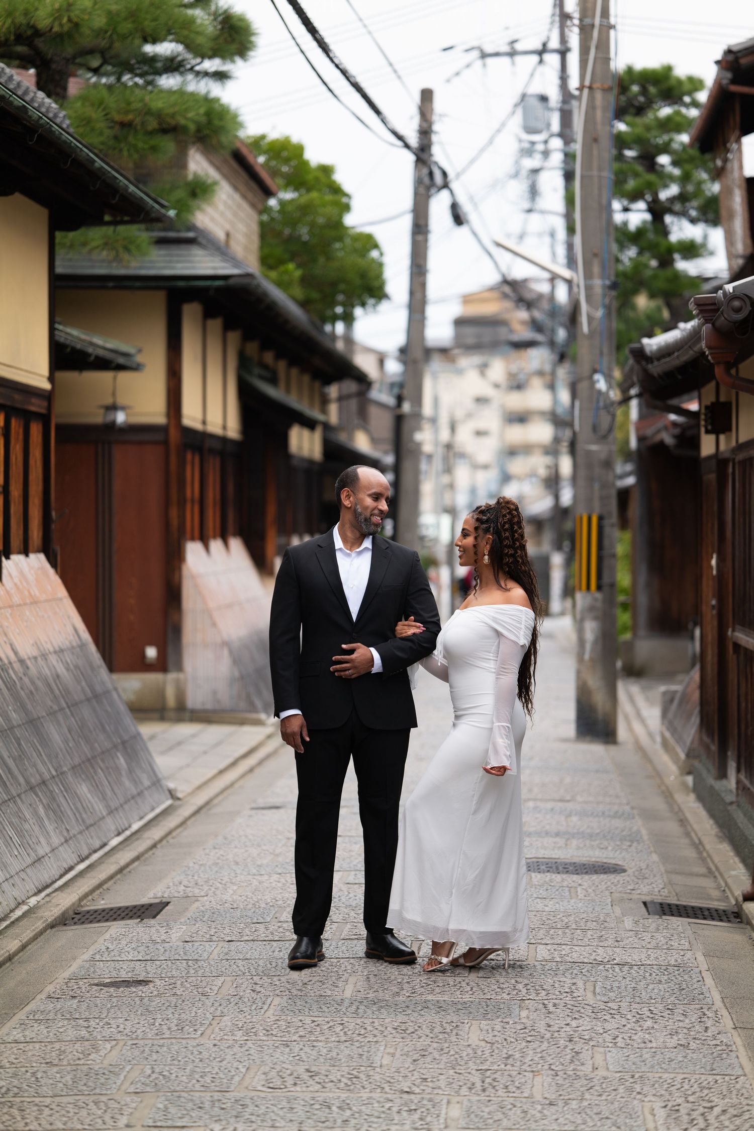 Elegantly dressed couple walking and smiling together on a traditional Japanese cobblestone street.