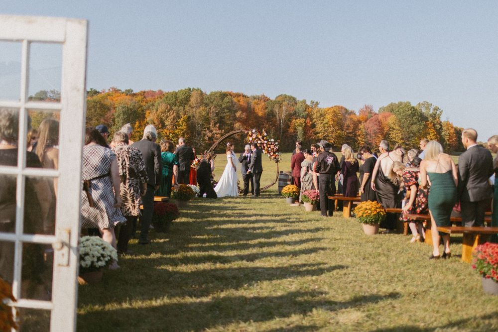 Wedding guests gathered on a hillside during an outdoor autumn ceremony.