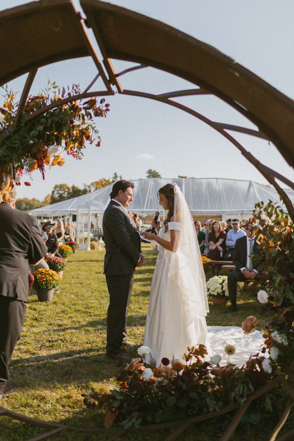 Wedding ceremony under a rustic wooden arch decorated with autumn flowers and greenery.