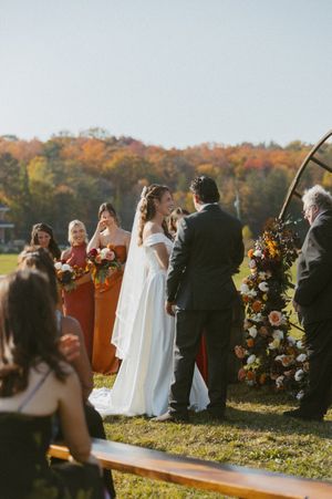 Outdoor wedding ceremony with burgundy bridesmaids dresses against autumn foliage.