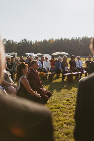 Wedding guests seated on a grassy hillside during golden hour with trees in the background.