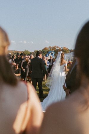 Wedding ceremony captured from behind guests' heads during golden hour.