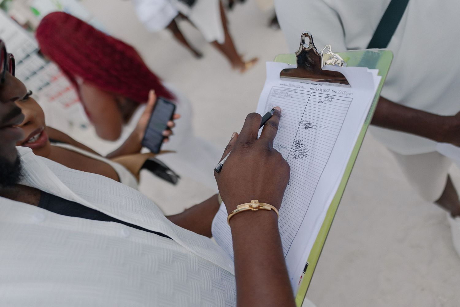 Student writing in a notebook while working on schoolwork at a desk with other papers and materials visible.