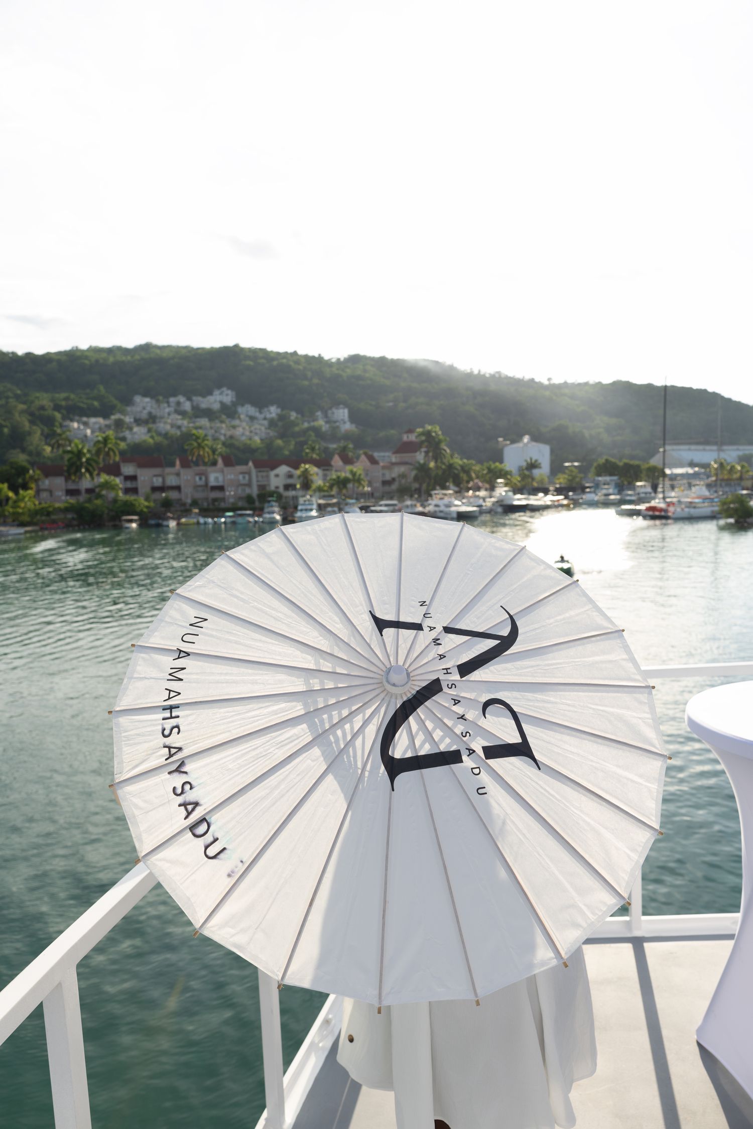 White parasols arranged in a row on a boat deck overlooking a scenic waterfront with hills in the background.