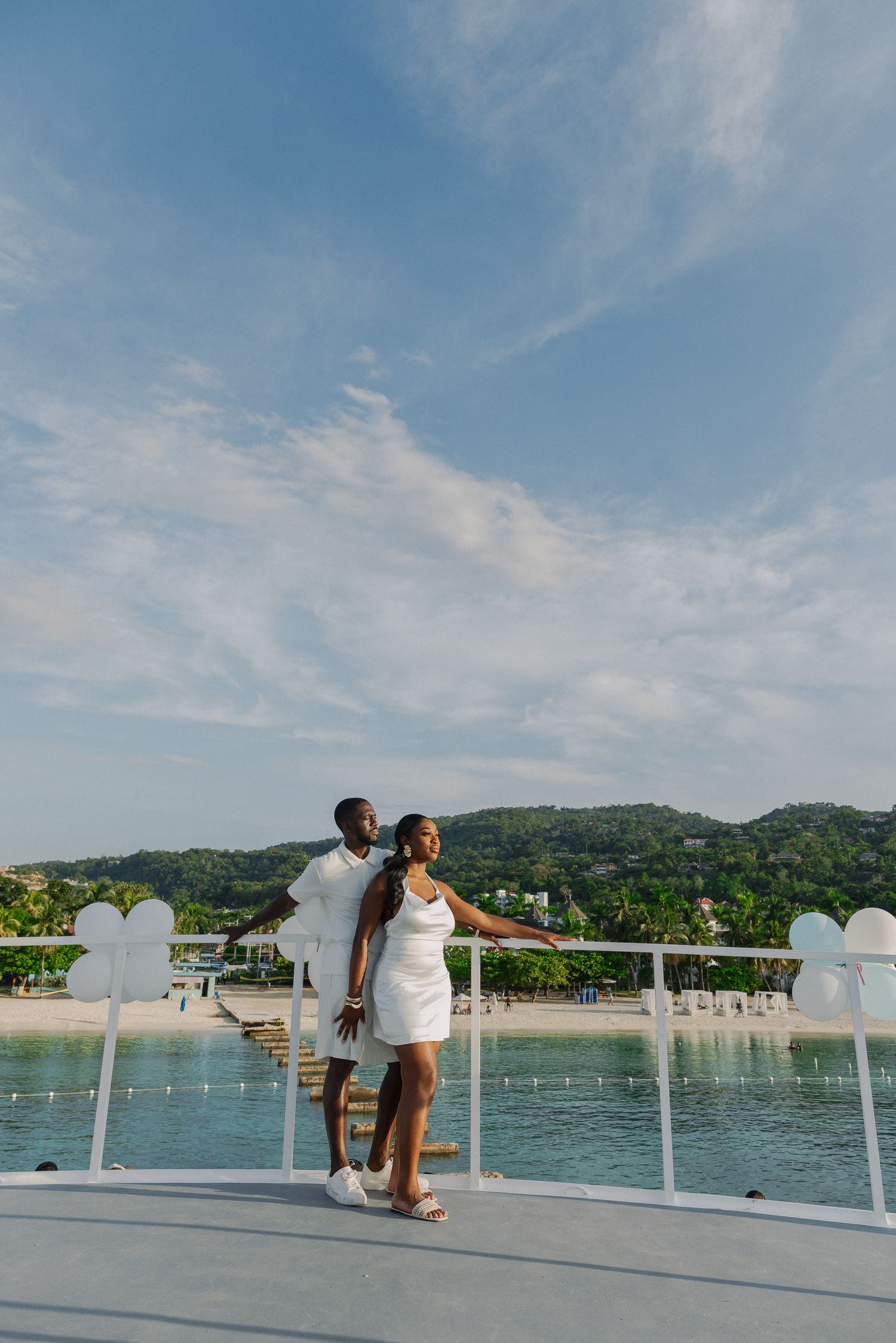 A romantic moment unfolds on a boat deck overlooking a scenic lake surrounded by green hills under a blue sky.