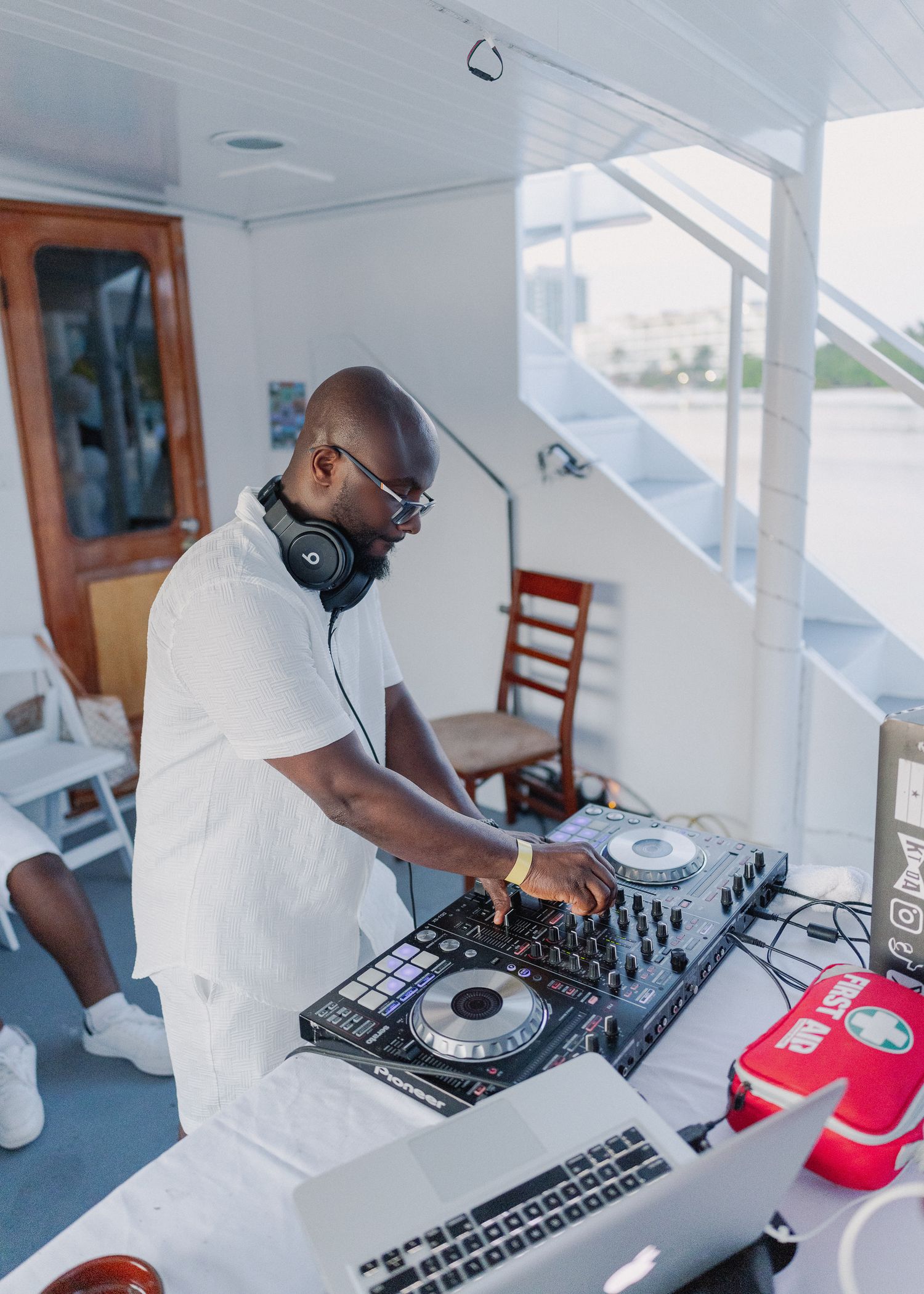 A DJ performs on professional mixing equipment at a bright indoor venue during a daytime event.