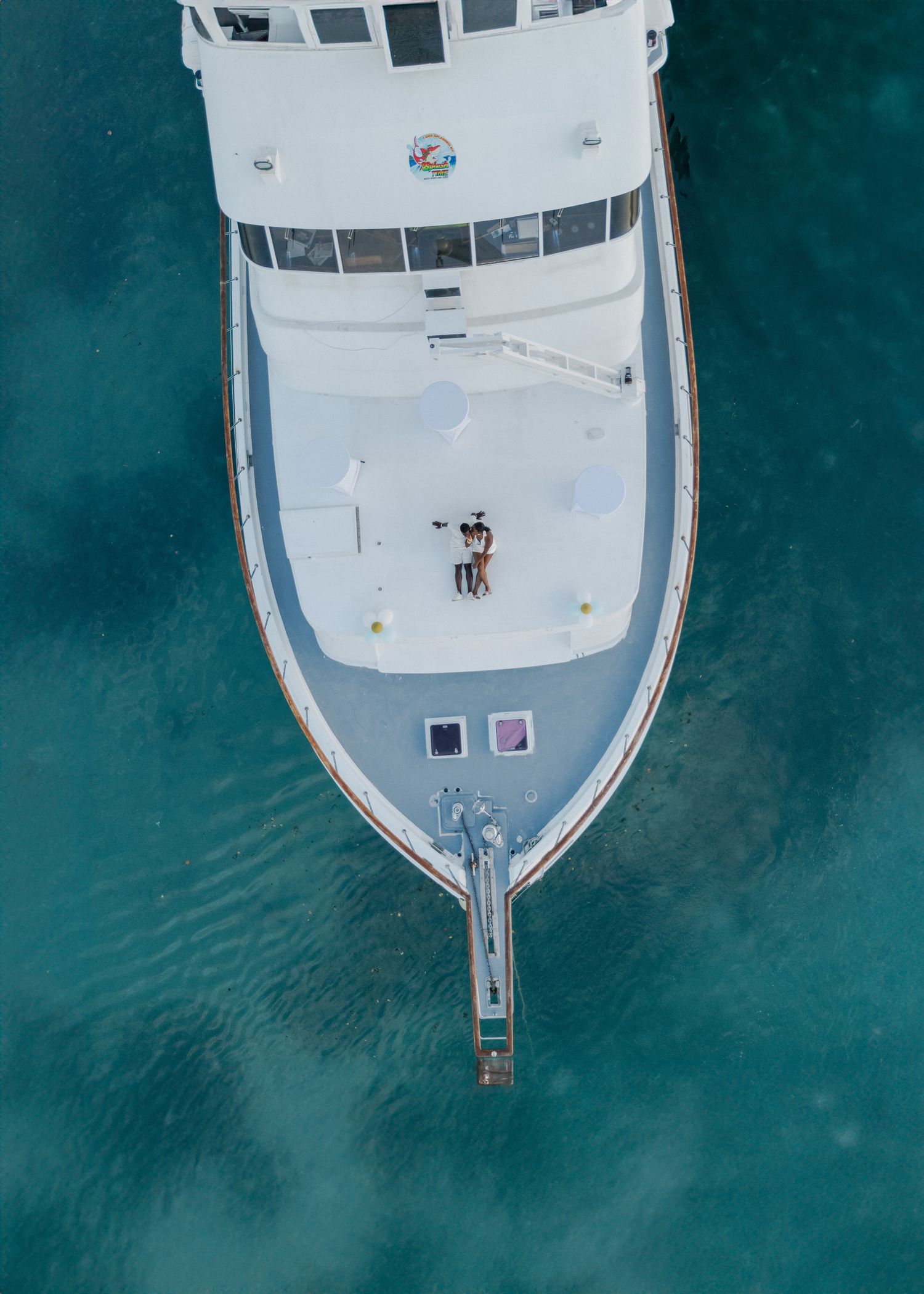 Bird's eye view of a white yacht's bow against crystal clear turquoise waters.
