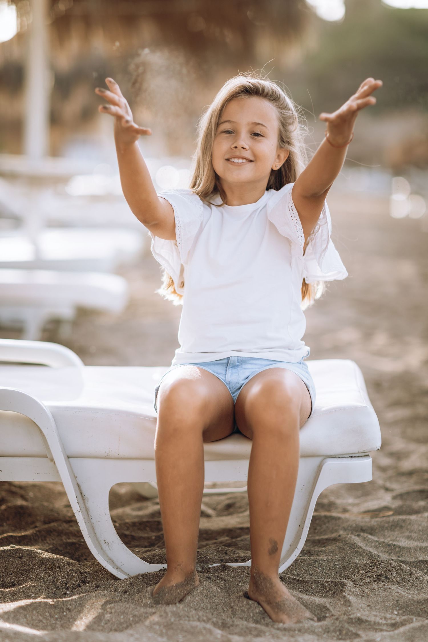 Happy child playing with sand while sitting on beach chair at sunset.