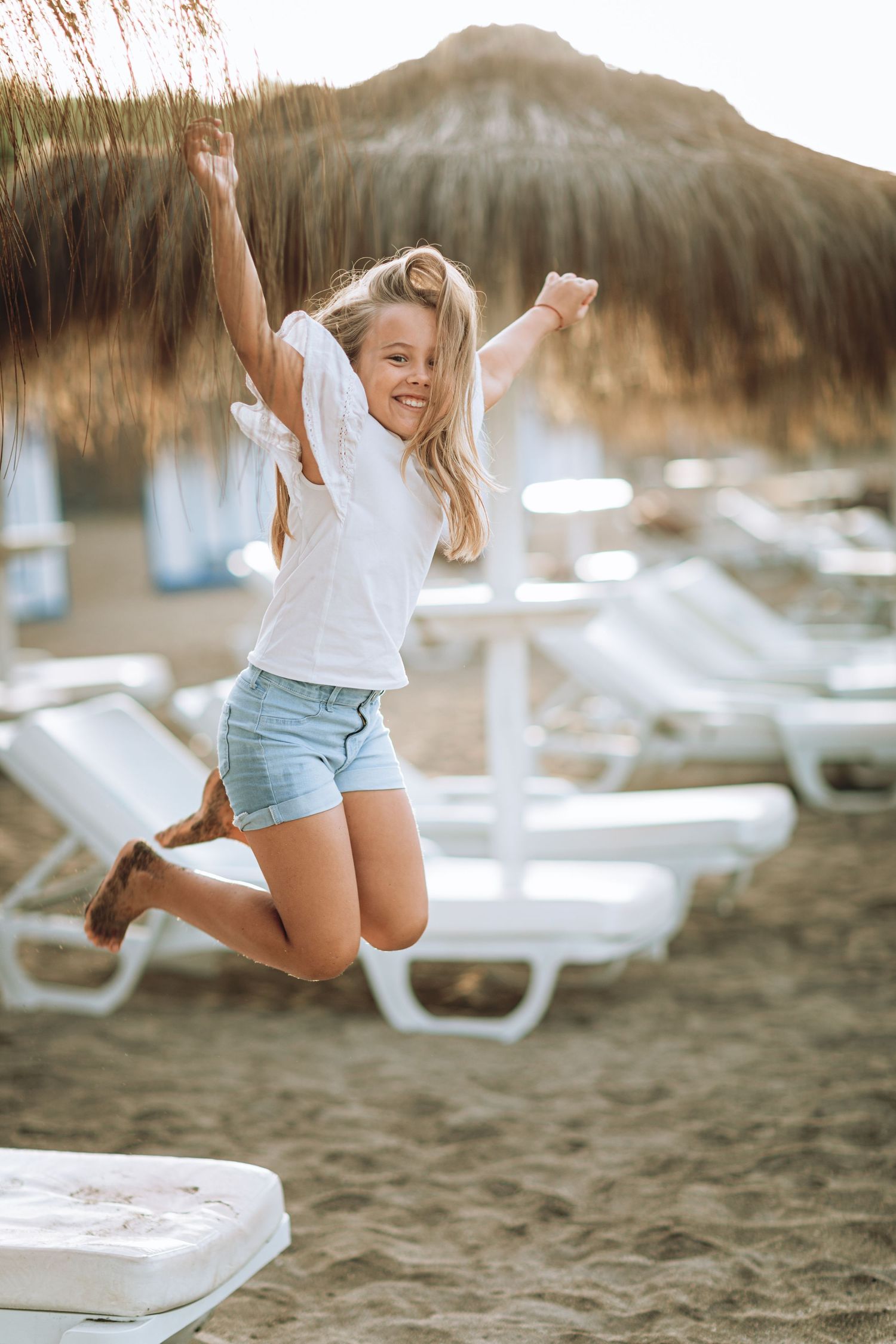 Person joyfully jumping on a beach with lounge chairs in the background.