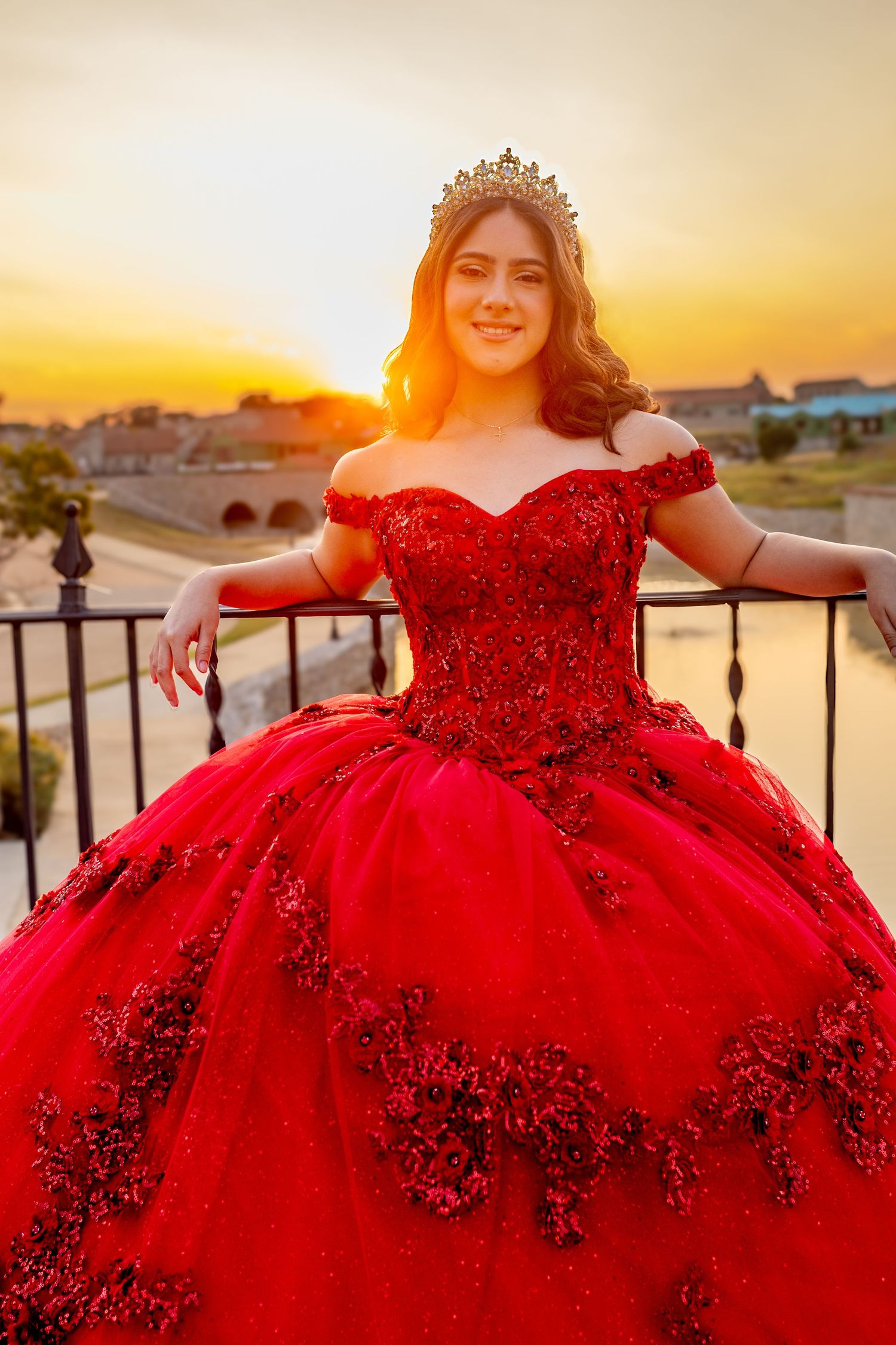 A stunning red ballgown with ruffled tulle skirt photographed at sunset against stone pillars and arches.
