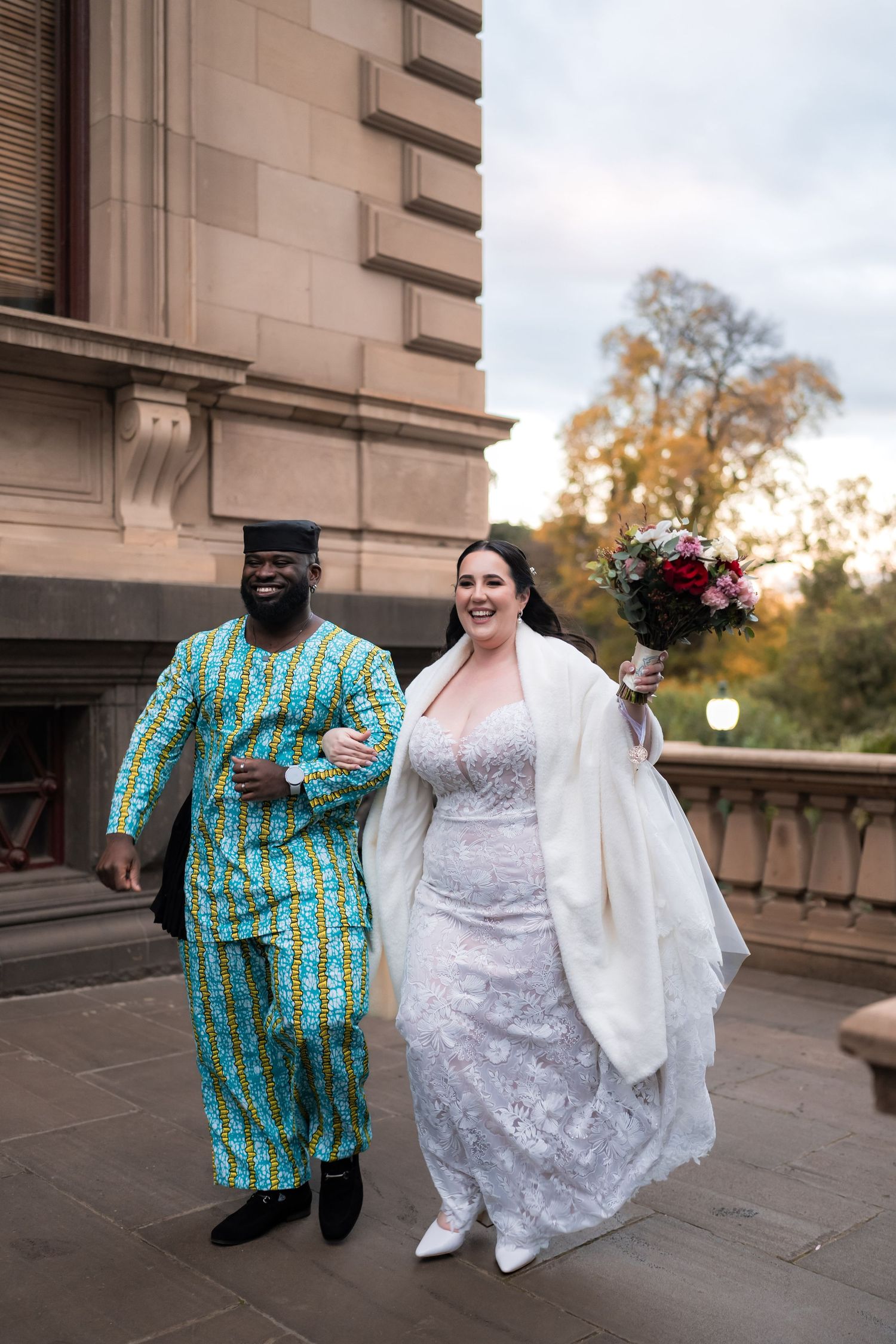 A couple in traditional African print and white wedding attire dance together during their outdoor wedding celebration.