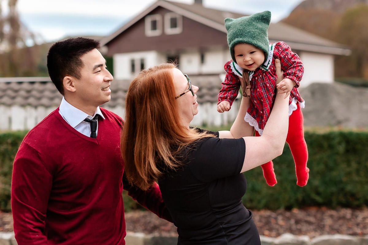 Mor, far og datter i finklær på julekortfotografering på Ålgård med Ørstavik Foto. Mor holder baby opp i luften mens far ser på og smiler.