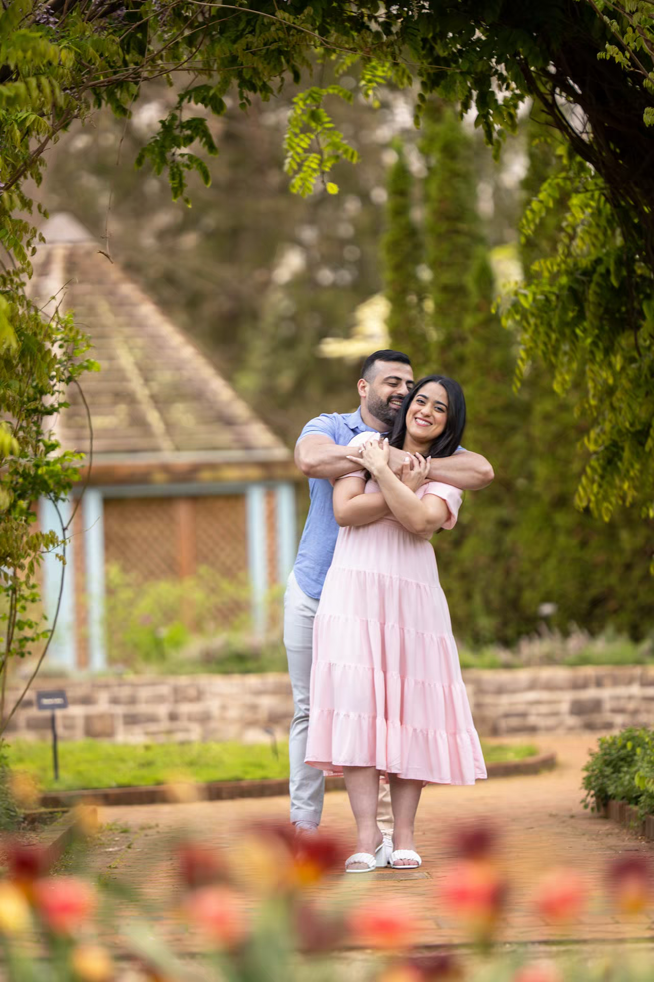 engaged playful couple embraces in a lush garden, at Inniswood Metro Gardens