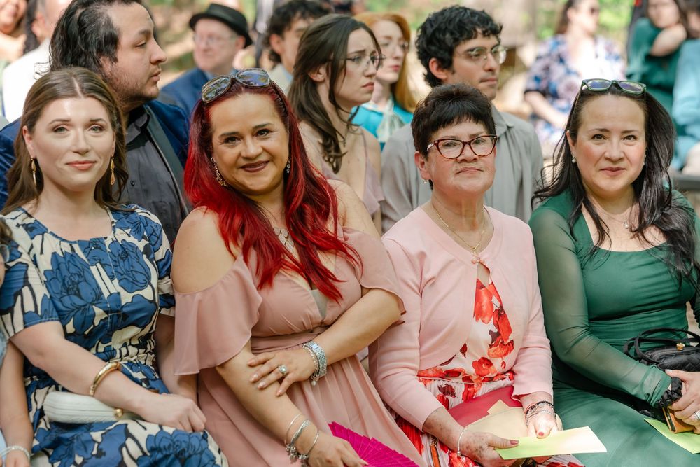 Four women guests smiling at outdoor wedding ceremony seated in audience.