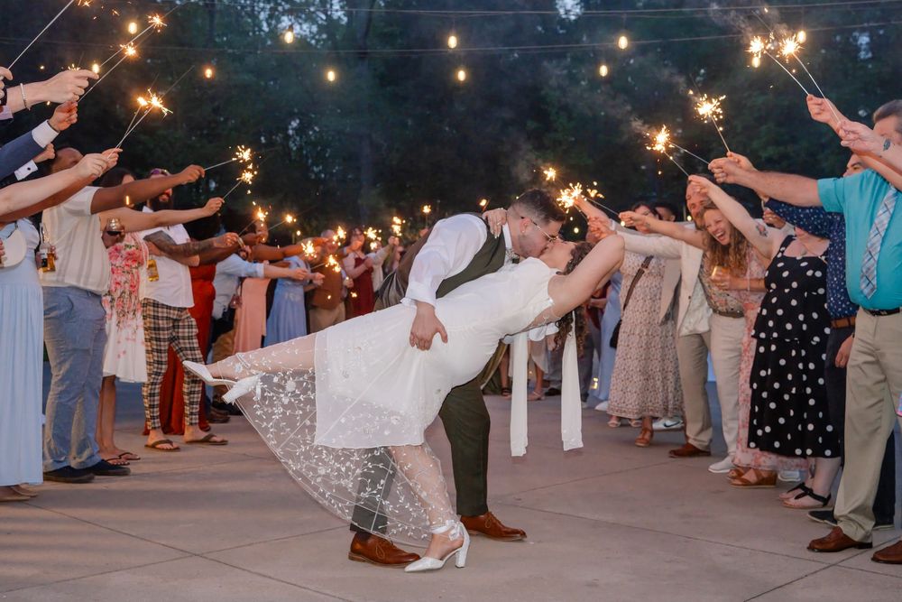 Groom dips bride during sparkler exit at outdoor wedding reception at night.