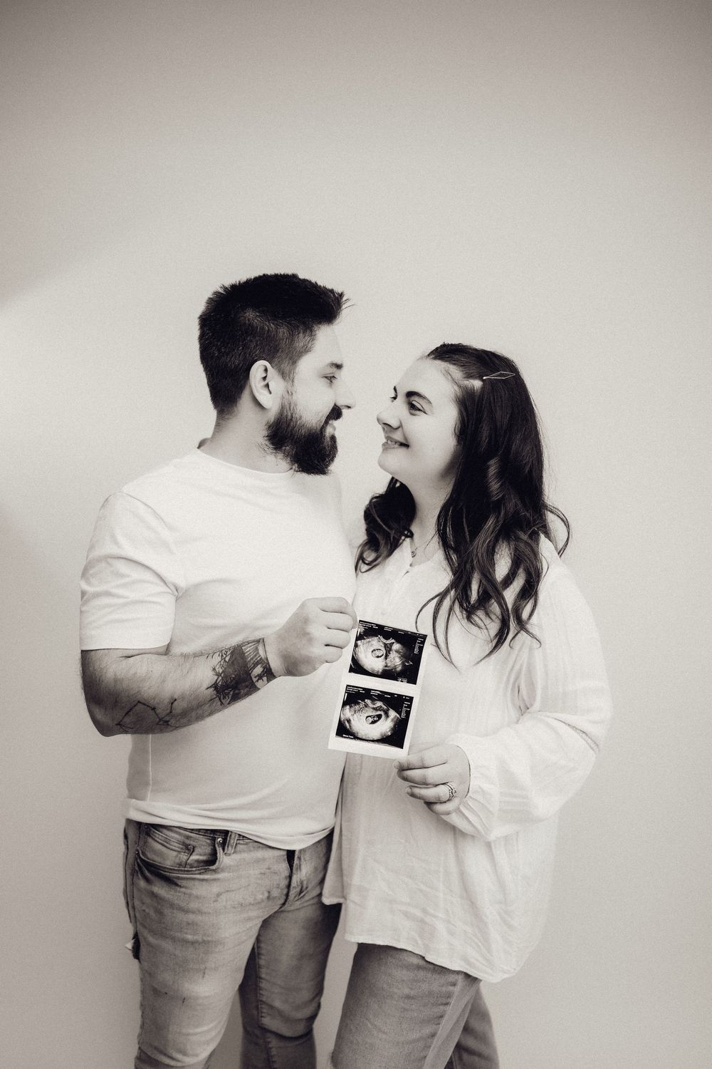 Black and white photo of couple smiling at each other holding ultrasound images.