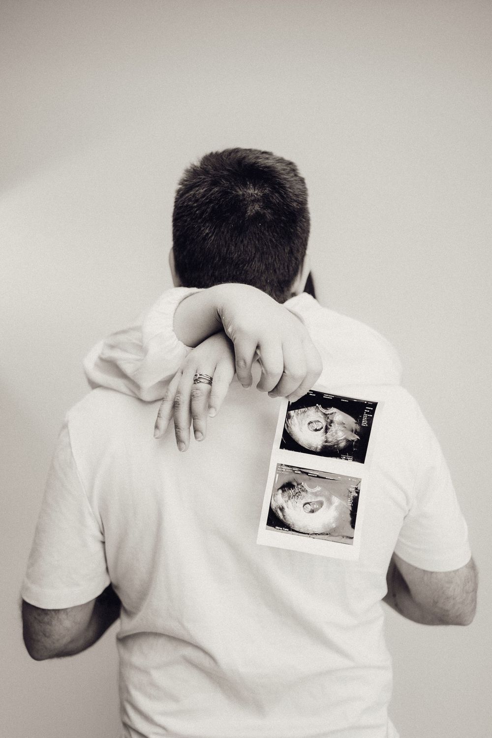 Man hugging woman from behind, woman holding ultrasound photos, black and white.