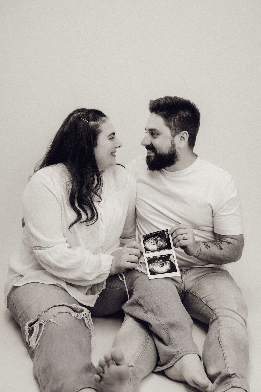 Black and white photo of couple sitting together laughing holding ultrasound scans.