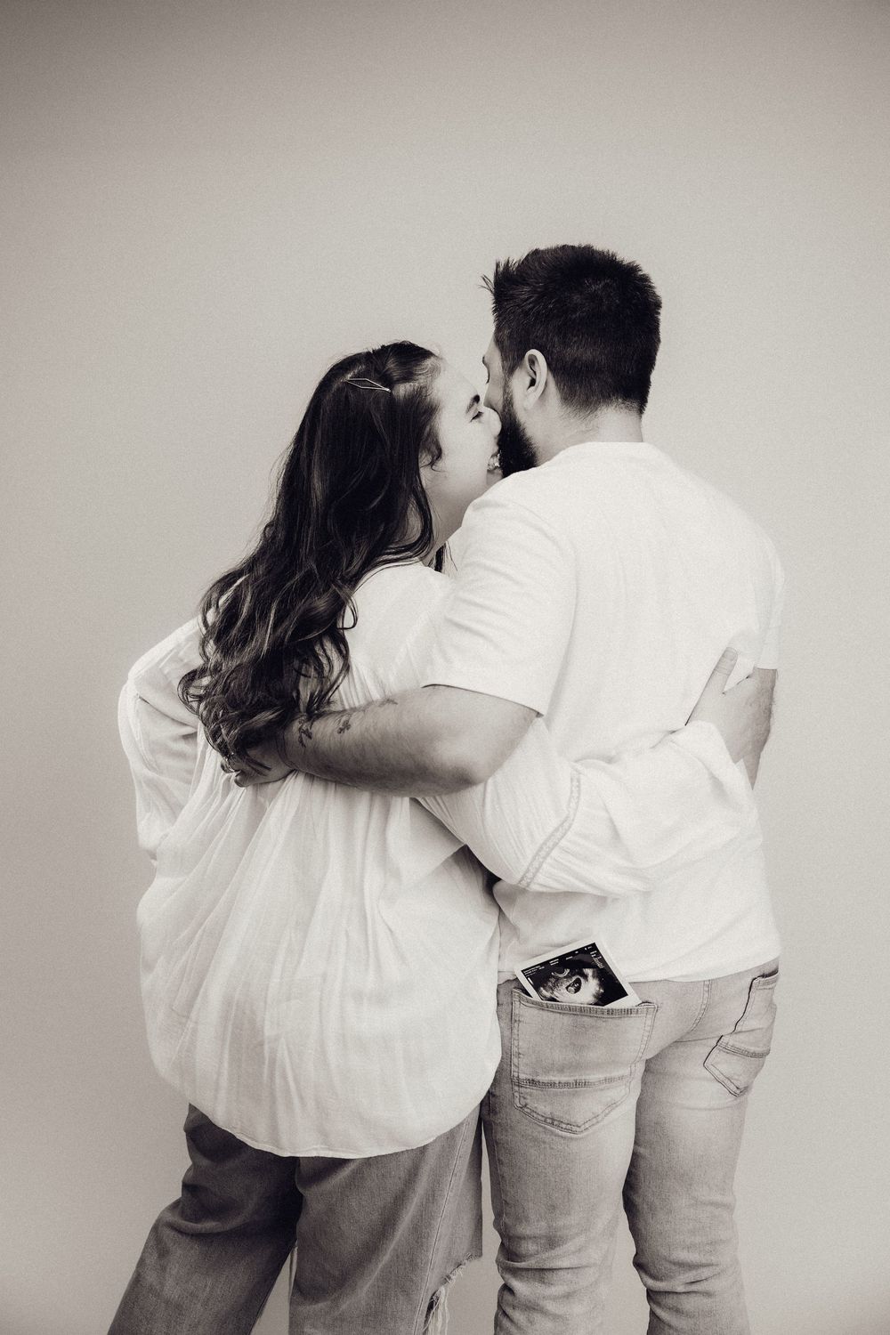 Black and white rear view of a couple embracing and kissing with ultrasound photo in mans pocket.