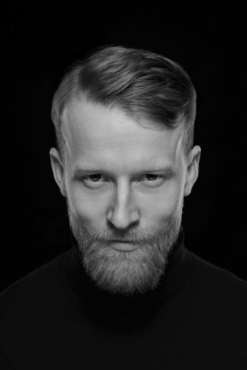 Czarno-biały portret brodatego mężczyzny z ułożonymi włosami, o poważnym wyrazie twarzy, na ciemnym tle. Zdjęcie biznesowe Lublin.